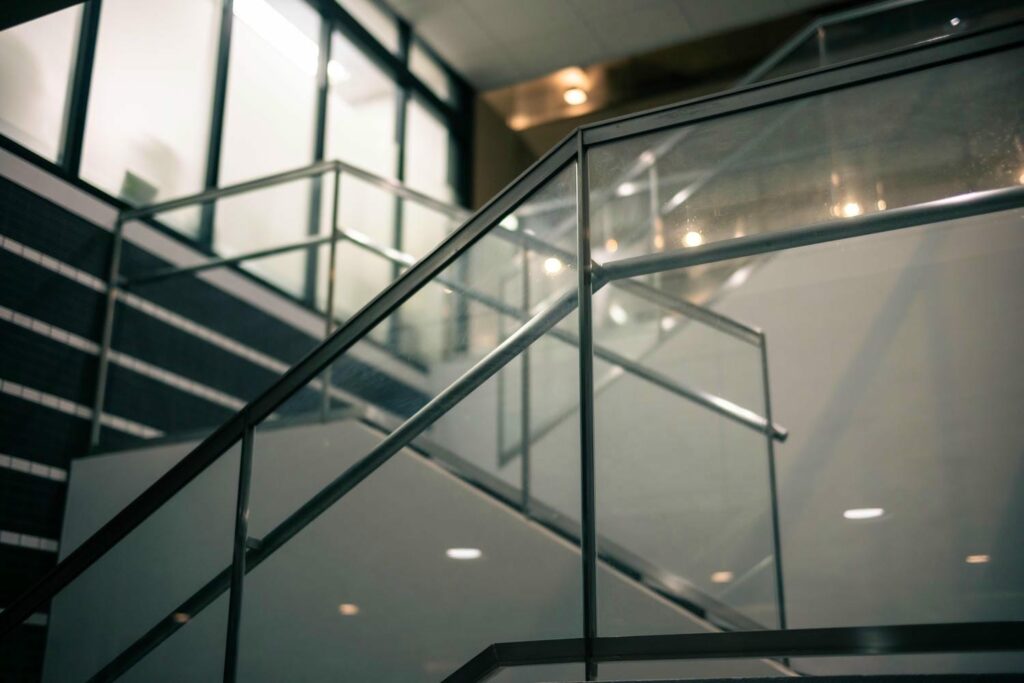 Close-up of an indoor glass stair railing showing the guard and handrail working together for safe stair use