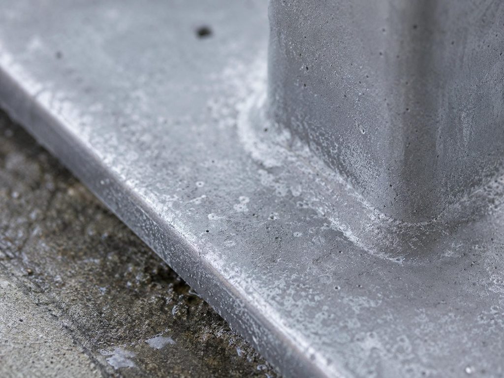 White powdery oxide and small pits on dull grey aluminum at the foot of a railing post