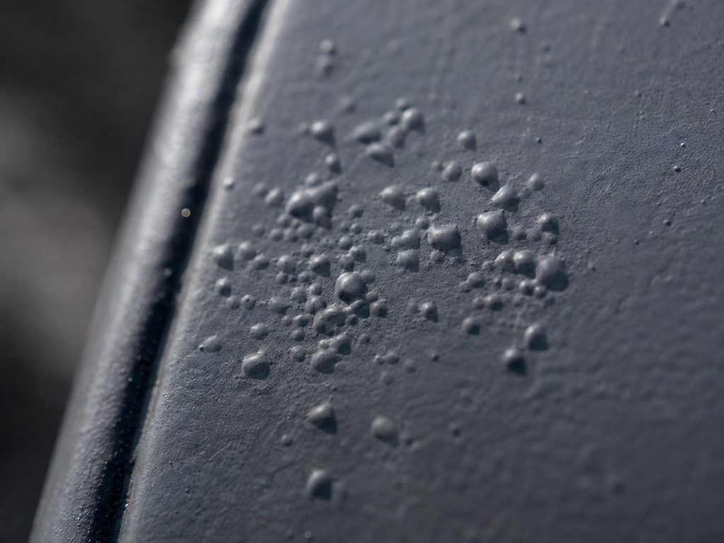 Small blisters and raised bumps under the dark powder coating on an otherwise intact metal railing