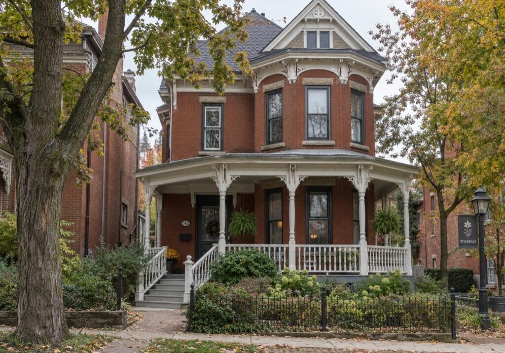 Red brick Victorian house in Toronto with a narrow wraparound covered porch and painted wood railings